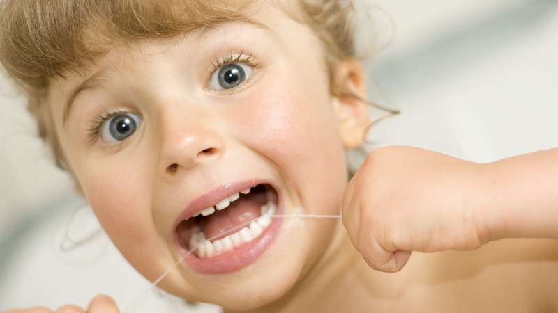 Criança limpando os dentes com o fil dental